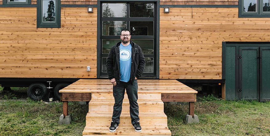 Sean Moroni in front of a wood-plank tiny home entrance.